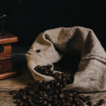 moedor de manivela ao lado de saco de tecido com grãos de café torrado, mostrando como moer café em casa sem moedor profissional