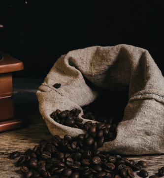 moedor de manivela ao lado de saco de tecido com grãos de café torrado, mostrando como moer café em casa sem moedor profissional