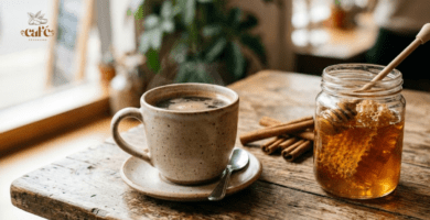 xícara de café sobre uma mesa de madeira; ao lado um pote de mel e paus de canela, exemplificando como adoçar o café naturalmente