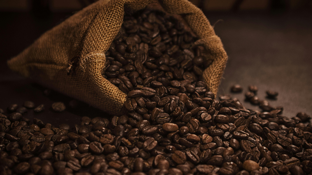 Saco de tecido cheio de grãos de café, derramando alguns grãos sobre a bancada, para ilustrar o post sobre Como Armazenar Café em Grãos para Manter o Frescor