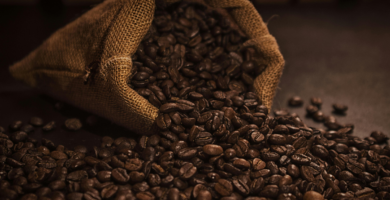 Saco de tecido cheio de grãos de café, derramando alguns grãos sobre a bancada, para ilustrar o post sobre Como Armazenar Café em Grãos para Manter o Frescor