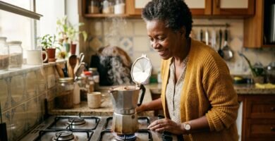 Mulher negra de cabelo grisalho observando o café subir na cafeteira italiana sobre o fogão