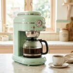 Cafeteira de design retrô em verde menta com jarra de vidro sobre bancada de mármore clara
